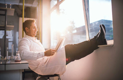 U.S. HealthTek scientist sitting in a chair with legs up on window shelf while reading documents