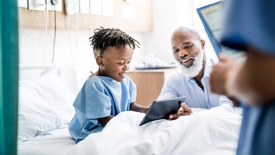 a young boy sitting in a hospital bed looking at a tablet