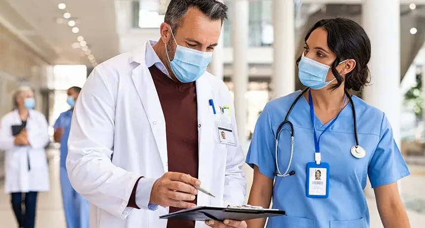 Two medical workers standing talking and pointing at a tablet.
