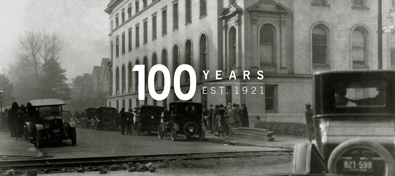 Old picture of a downtown street with cars with 100 years Est. 1921 written on top.