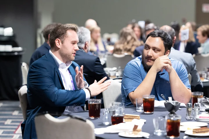 2 Executive War College attendees from the Clinical Laboratory and Pathology industries sitting at a lunch table with hundreds of other attendees behind them